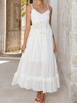 Eine Frau in einem weißen Spitzenkleid steht vor einer Steinmauer.