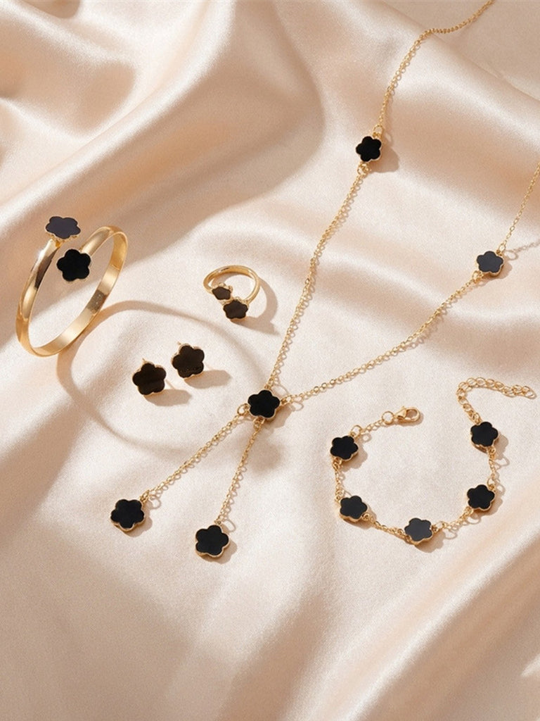 Goldfarbenes Schmuckset mit schwarzen, blütenförmigen Steinen auf beigefarbenem Stoffhintergrund
