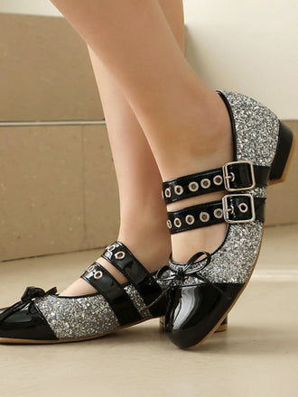 Schwarze und silberne Glitzerschuhe mit Schnallen auf neutralem Hintergrund
