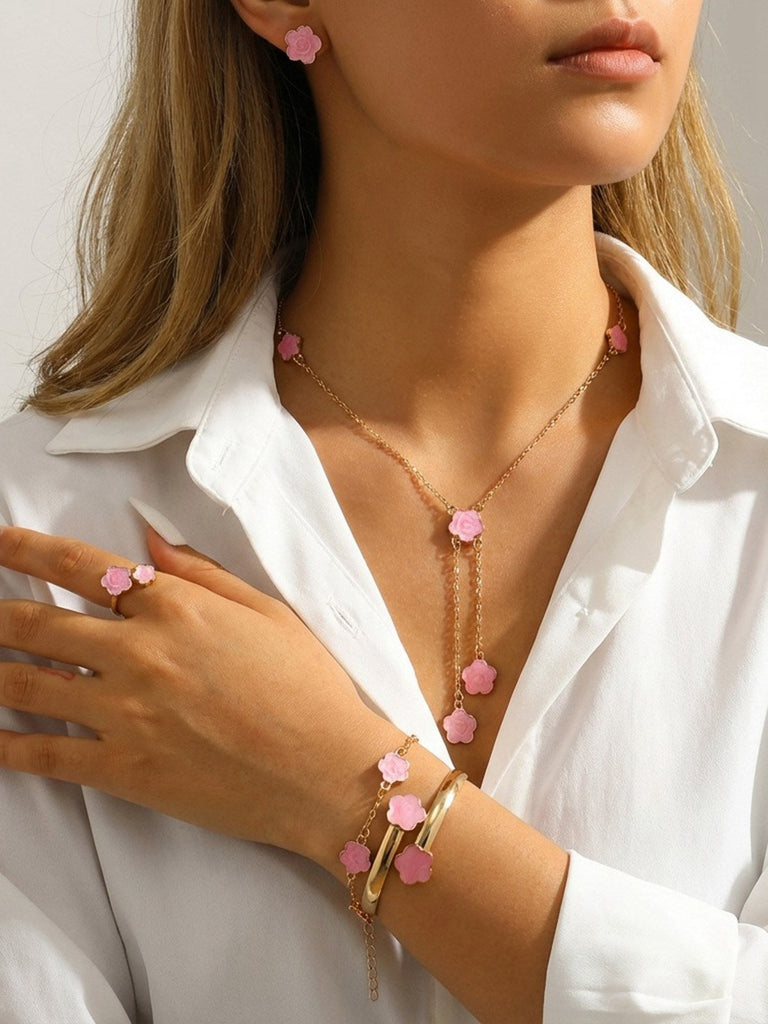 Person, die vor weißem Hintergrund eine rosa Halskette mit rosa Blumenanhängern, einen passenden Ring und ein Armband trägt.
