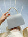 Silberne Clutch mit Perlmuttgriff, von einer Hand gehalten, vor hellblauem Hintergrund