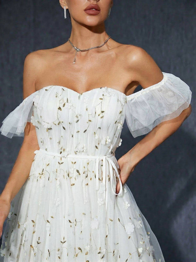 Frau in einem weißen, geblümten, schulterfreien Kleid vor dunklem Hintergrund