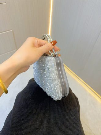 Hand hält eine silberne Perlenclutch vor neutralem Hintergrund
