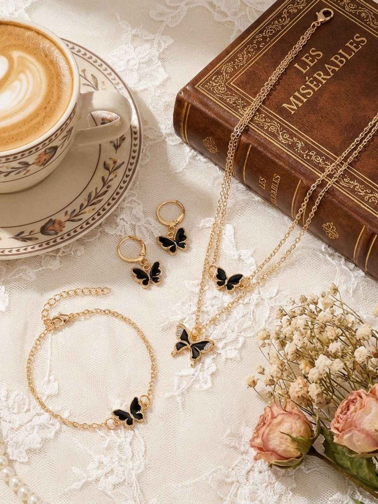 Schmuckset mit Schmetterlingsmotiven auf einer Spitzentischdecke mit einem Buch und einer Tasse Kaffee.