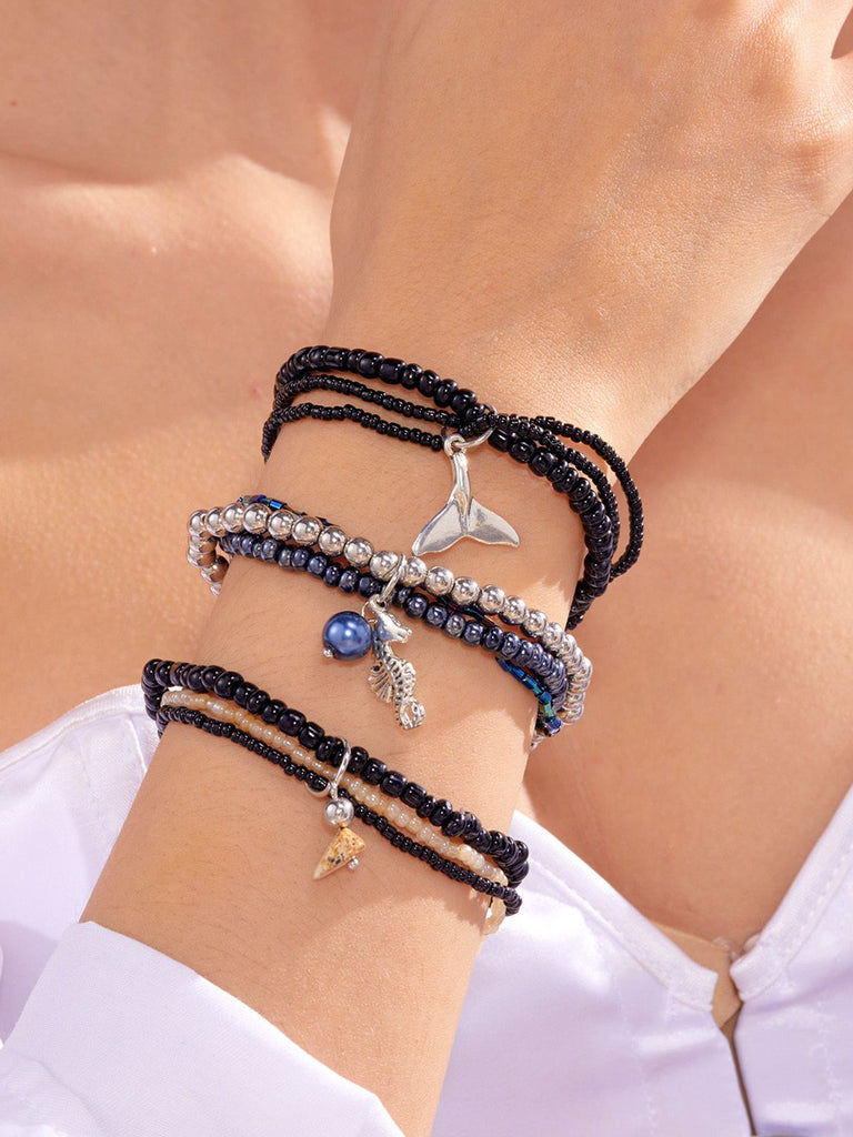 Mehrere Armbänder mit Anhängern an einem Handgelenk vor hellem Hintergrund