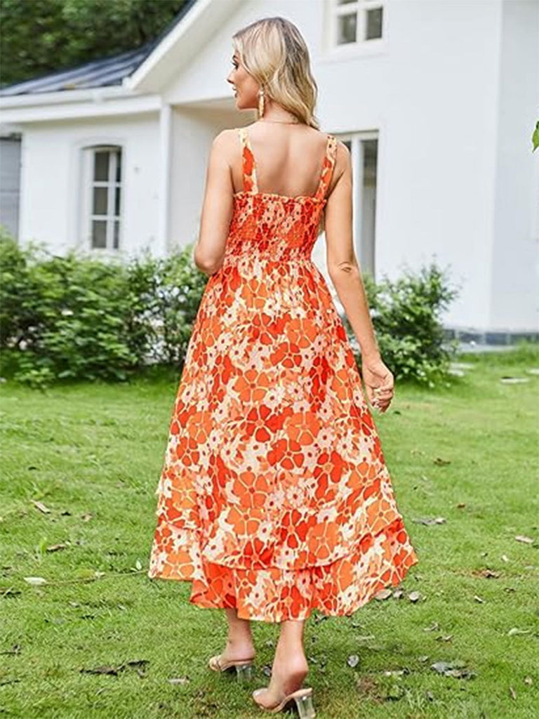 Eine Frau in einem orangefarbenen Blumenkleid steht auf einer Rasenfläche; im Hintergrund ist ein weißes Haus zu sehen.