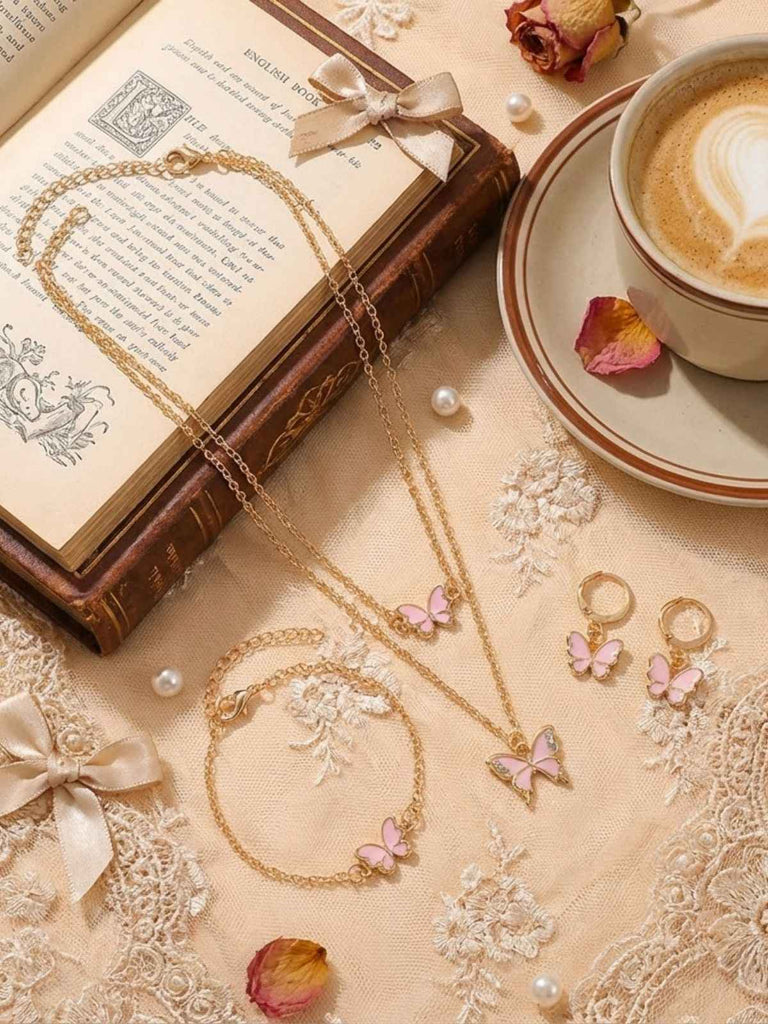 Eine goldene Schmetterlingskette liegt auf einer Spitzentischdecke, daneben ein Buch und eine Tasse Kaffee.