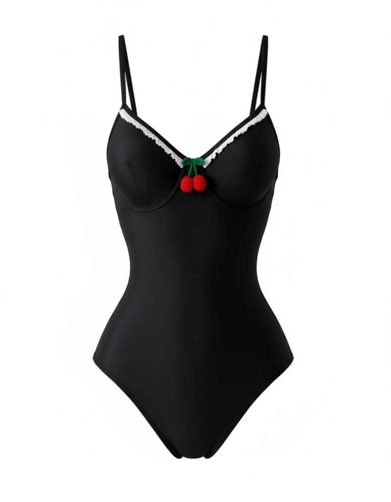 Studioansicht von vorne auf den schwarzen Badeanzug im Pin-up-Stil, der die kontrastierenden Zierborten und die kirschroten Akzente hervorhebt.